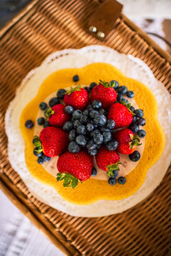 A colorful berry tart and white doily atop a wicker table, seen from above