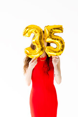 Beautiful woman with balloons and the numbers 35 is photographed in the studio in a red dress....