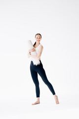 Beautiful and slender woman in a short sports top stands with a mat in her hands, on a white background, copy space