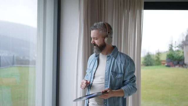 Man listening to vinyl with headphones, enjoying music, dancing. Pairing turntable with pair of wireless headphones at home.