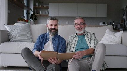 Father and son looking at photos in photo album, reminiscing about the son's childhood and family, recalling the old days.
