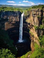 Obraz premium A waterfall is flowing down a cliff, surrounded by lush green trees. The scene is serene and peaceful, with the sound of the water creating a calming atmosphere