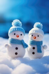 Two snowmen with blue hats and scarves are standing on a snowy field. The scene is peaceful and serene, with the snowmen looking like they are enjoying the winter weather
