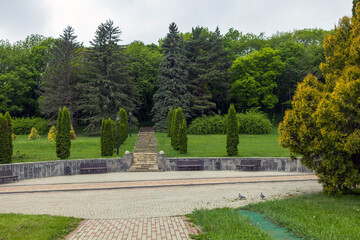 A beautiful landscaped park with benches, paths and green lawns, a gazebo in the morning in the fog.