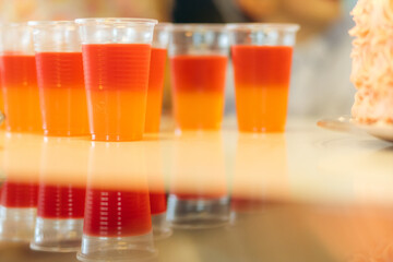 Multiple cups of red and orange jello next to each other on a counter, reflecting in the counter surface