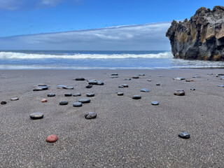 Turquoise blue sea water with white foam on waves. Beach with black volcanic sand and stones. Close up photo. Tenerife, Puerto de la Cruz