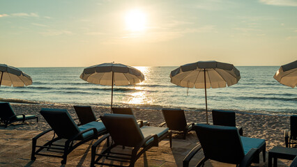 Sunset beach scene with empty lounge chairs and umbrellas facing ocean, capturing serene evening...