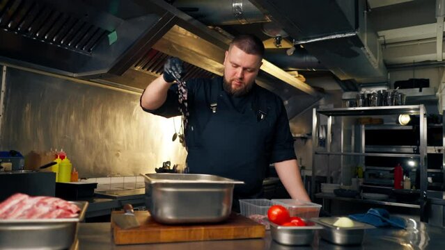 in professional kitchen in a chef in a black jacket salts and peppers ribs in an iron bowl