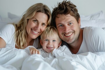 Fototapeta premium Happy family of three embracing and smiling in bed with white bedding, capturing a moment of love and joy.