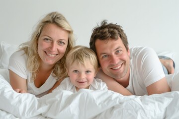 Obraz premium Happy family of three lying on a bed smiling and enjoying their time together, captured in a bright and cheerful setting.