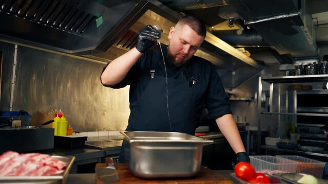 in professional kitchen in a chef in a black jacket pours oil into vegetables in an iron bowl