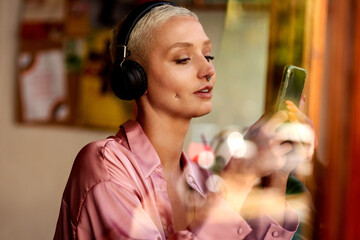Woman, phone and headphones in cafe, social media and listening to music on app to relax. Female...