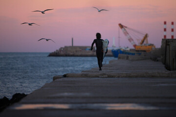 surfer running along pier just after sunset with port and ocean in background