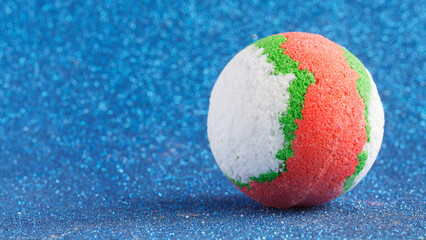 Large, multi-colored, red, white and green bath bomb on a sparkling blue background, simulating...
