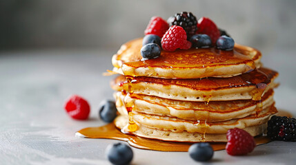 A stack of fluffy, golden pancakes, drizzled with maple syrup and adorned with fresh berries, showcased against a clean, white surface to accentuate their mouthwatering appeal.