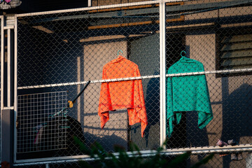 Two orange and green shirts hanging on a fence. The fence is made of metal and is attached to a...