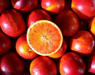 Juicy Tarocco blood orange cut in half on top of a bed of whole red oranges.