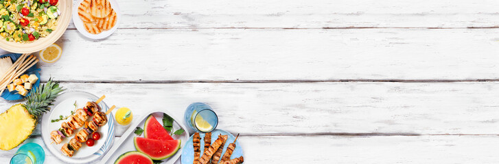 Summer food corner border with  meat skewers, salad, fruit and snacks. Top down view on a white wood banner background. Copy space.