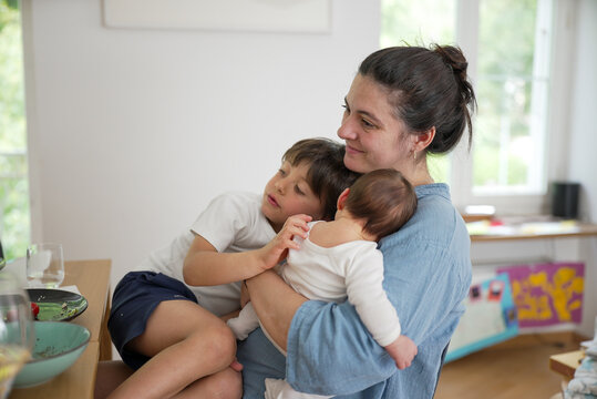 Mother with baby and young child, balancing care and attention between them, showcasing the tender moments of motherhood and the challenges of multitasking in a loving family setting