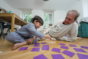 Elderly man and young boy playing a memory game on the floor, engaging in fun and educational...