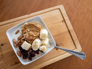 Top view of healthy oatmeal with peanut butter, bananas and cranberries served in a white bowl on a...