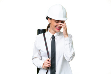 Young architect woman with helmet and holding blueprints over isolated background laughing