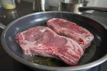 Raw ribeye steaks sizzling in a hot pan, beginning the cooking process, highlighting the marbling...