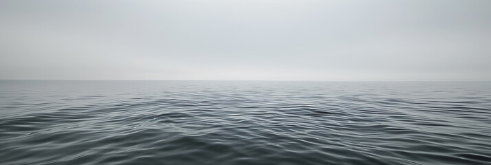 Vast, calm ocean under a gray sky, with gentle waves creating a serene and tranquil seascape.