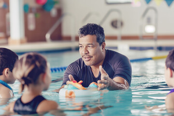 Swimming coach instructing young children in pool during lesson. Engaging and supportive environment promoting water safety and learning