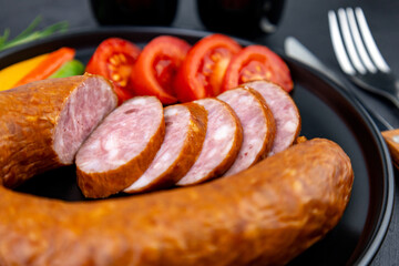 Pieces of salami sausage with tomatoes on a black plate