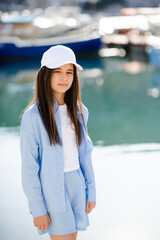 Cute stylish teenage girl 10 - 12 year old wearing cap and blue shirt with shorts over sea and...