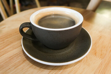 close up of black mug cup with hot black americano coffee on a wooden table.