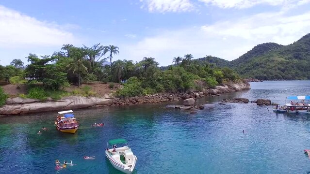 Barcos, lanchas, veleiros e iates ancorados em ilha tropical paradis&iacute;aca em Paraty, Rio de Janeiro, Brasil. Imagens a&eacute;reas de drone sobrevoando o mar e diversos turistas tomando banho e se divertindo