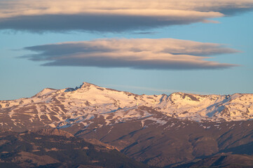 Fototapeta premium Huge lenticular clouds over the snowy peaks of the Sierra Nevada in Granada (Spain) at sunset