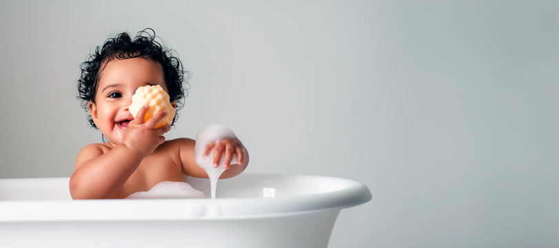 Biracial baby girl playing with a sponge in a modern white bathtub