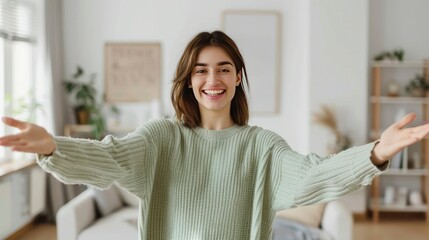 woman with open arms facing the camera, on a white background, wearing a light green sweater.