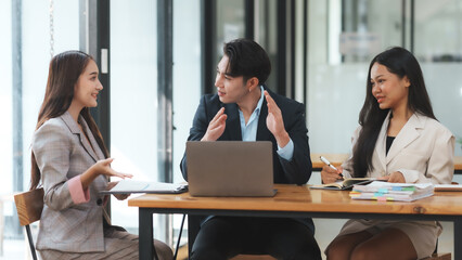 Three business colleagues are having an animated discussion, with expressive gestures and engaged expressions, while reviewing documents in a modern