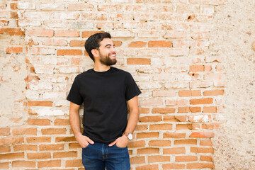Smiling young hispanic man casually dressed in a plain black t-shirt stands against a textured...