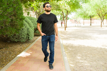 Young hispanic man wearing a plain black t-shirt for mockup, strolling outdoors, ideal for apparel...