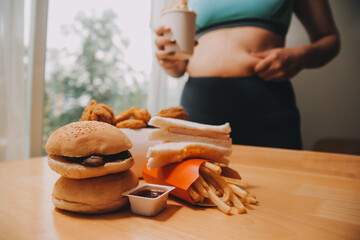 To eat or not. Cheerless plump woman looking at the burger while thinking to eat it or not