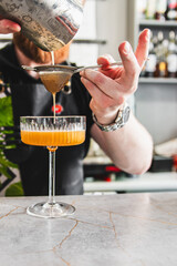 A skilled bartender pours a cocktail through a strainer into an elegant glass on a bar counter