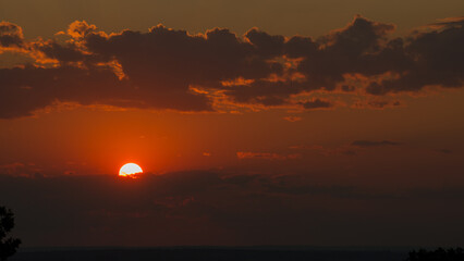 Fototapeta premium Red solar disk at the sunset and dark rain clouds on the horizon.