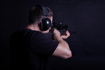 Young man with ear and eye protection shooting a rifle against a black background