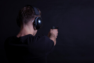 Young man with ear and eye protection shooting a pistol on a black background
