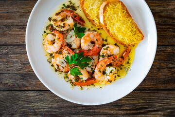 Fried shrimps with garlic and parsley in olive oil and toasted bread on wooden table
