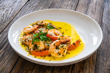 Fried shrimps with garlic and parsley in olive oil and toasted bread on wooden table
