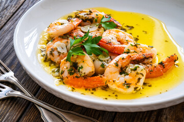 Fried shrimps with garlic and parsley in olive oil and toasted bread on wooden table
