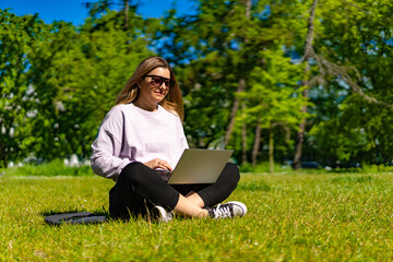 Beautiful woman using laptop sitting on grass in city park
