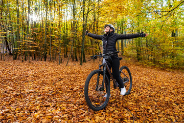 Mid-adult woman riding bicycle in city forest in autumnal scenery
