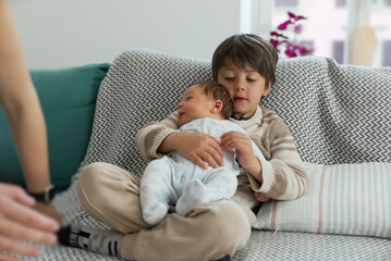 Older brother holding his baby sibling on a cozy couch, depicting a tender moment of sibling bonding and love in a comfortable home setting